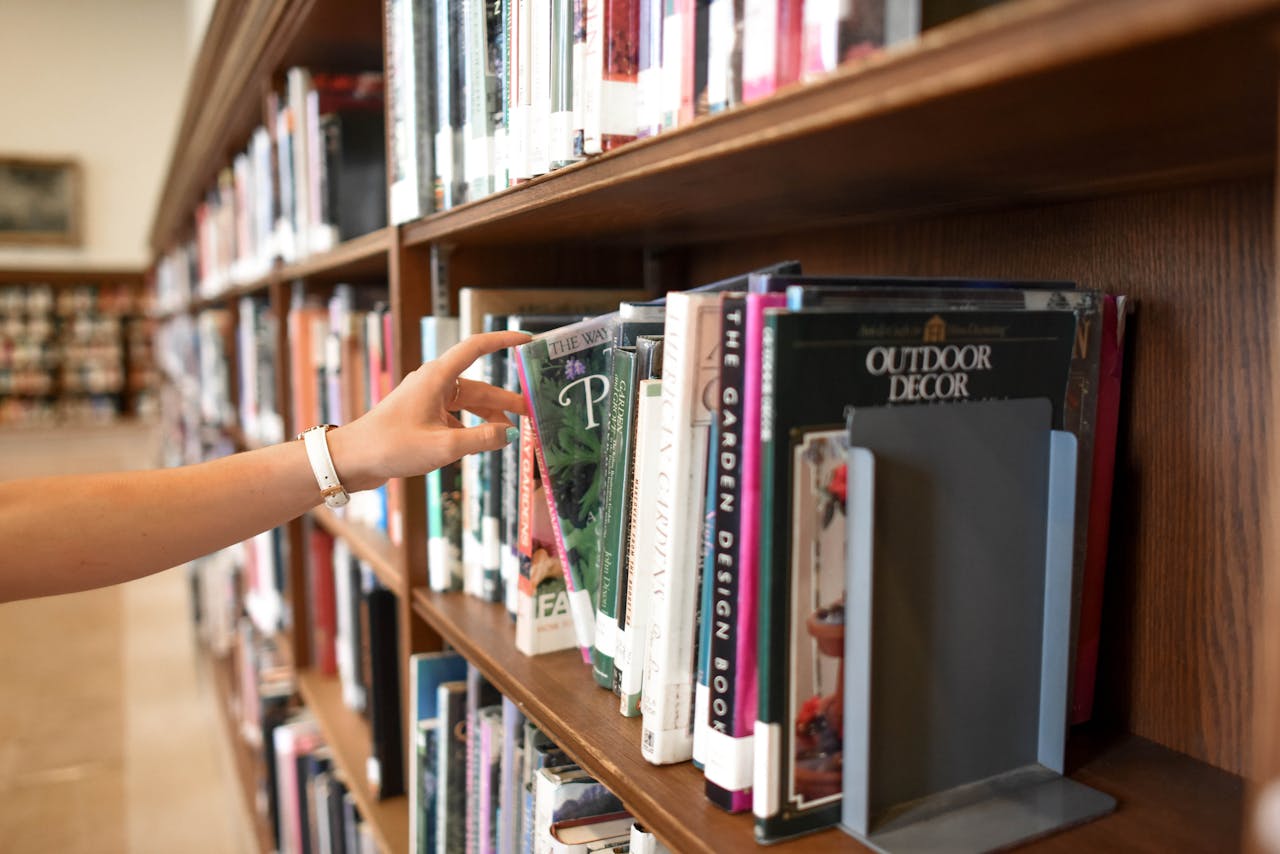 A close-up of a persons hand reaching for a book in a library shelf, suggesting exploration and learning.