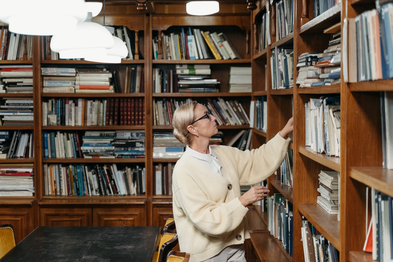 Woman exploring a library bookshelf with a thoughtful expression, surrounded by books.