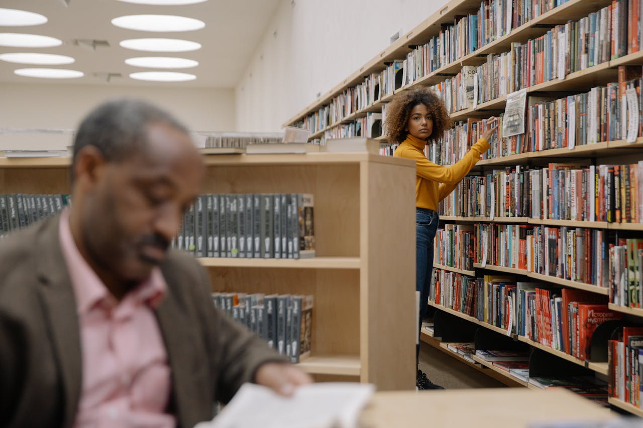 Two people engrossed in books within a spacious library setting.